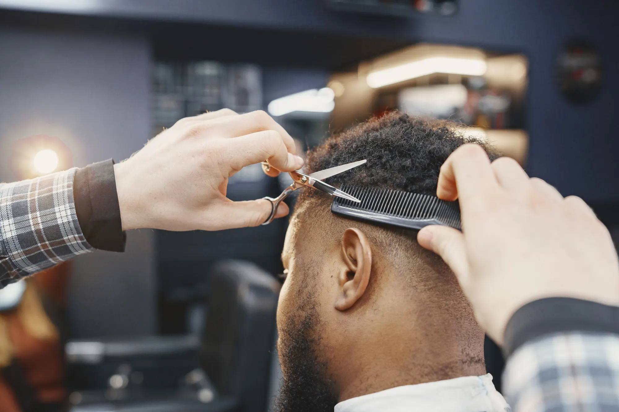 A barber shaping a client's hair with scissors and a comb